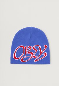 Gorro de punto en azul vibrante con gran texto bordado en rojo "OBEY" en una fuente estilizada, con textura suave y diseño ajustado.