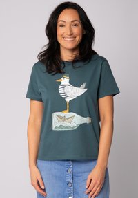 Türkiser Baumwoll-T-Shirt mit einem Grafikdesign eines Möwen in einem gestreiften Hemd, die auf einer Flasche steht, in der ein Papierboot ist.