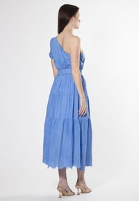 Blauwe katoen midi-jurk met één schouder, geplooide lijfje, gelaagde rok en geborduurde details aan de zoom, gecombineerd met beige hoge hakken.
