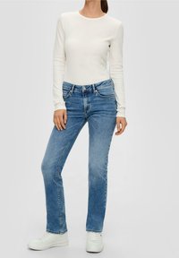 Bílý dlouhý rukáv ribbovaný top spárovaný se světle modrými džíny rovného střihu. Džíny mají pět kapes a jsou nošeny s bílými teniskami.