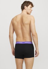 Schwarze Boxer-Shorts mit einem lila Bund, auf dem das Logo "JACK & JONES" zu sehen ist. Glattes Material und enganliegende Passform, von hinten gezeigt.