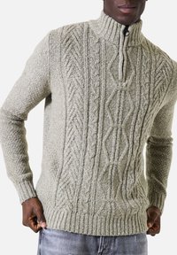 Lichtgrijze gebreide trui met een hoge kraag, gekenmerkt door een getextureerd kabelbreipatroon en ribbels aan de mouwen en onderrand. Voorzijde met ritssluiting.