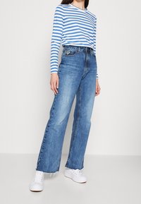 Modrá a bílá pruhovaná košile s dlouhým rukávem, spárovaná se světle modrými širokými džíny. Bílé tenisky dokončují outfit.