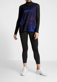 Top senza maniche Nike di colore blu scuro con texture in rete, logo grafico, abbinato a leggings neri e sneakers bianche.