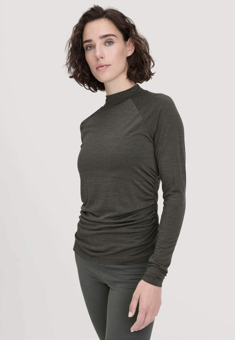 Langärmliges, dunkelgrünes Oberteil mit hohem Kragen, das an den Seiten gerafft ist und eine glatte Textur aufweist. Kombiniert mit schmal geschnittenen Hosen für einen eleganten Look.