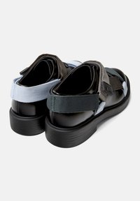 Zapatos de plataforma negros con correas elásticas en azul, gris y verde. El diseño cuenta con un empeine suave y una suela texturizada.