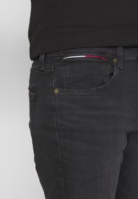 Jeans de mezclilla negra con un corte ajustado, que presentan herrajes dorados, un bolsillo frontal con un acento de color y detalles de costura sutiles.