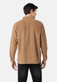 Brown corduroy shirt with long sleeves, buttoned cuffs, and a classic collar, featuring a textured surface and a relaxed fit.