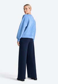 Light blue cotton sweatshirt with raised lettering on back, paired with navy wide-leg pants and black shoes. Smooth texture, casual design.