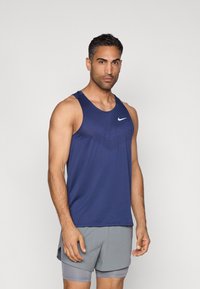 Maiou sport albastru închis, din material ușor, cu un model texturat și logo-ul Nike swoosh. Asortat cu pantaloni scurți gri.