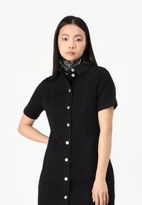 Vestido preto de manga curta com um decote tipo colarinho, botões frontais e costuras laterais. Combinado com um lenço com padrão preto e branco.
