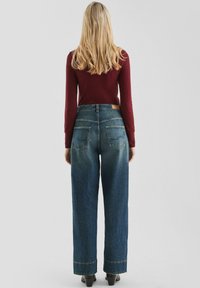 Jeans z wysokim stanem, luźne, niebieskie dżinsy z surowym dołem, tylne kieszenie i skórzaną metką w pasie. Noszone z dopasowaną bordową bluzką.