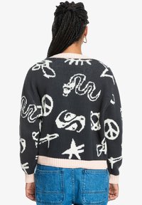 Knitted sweater in dark gray with white patterns, featuring peace signs, snakes, and other motifs. Ribbed pink hem and cuffs.