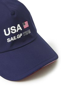 Mørkeblå baseballcap med hvid "USA SAILGP TEAM" tekst og amerikansk flag. Glat stof, buet skygge, rød underside af skyggen.