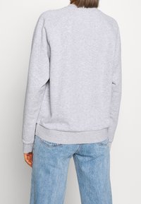 Sudadera gris de mezcla de algodón, con dobladillos y puños acanalados. Presenta un ajuste relajado y mangas raglán, con una textura suave.