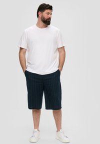T-shirt blanc à manches courtes associé à un short navy à rayures. Le short a une coupe décontractée et est accompagné de baskets blanches.