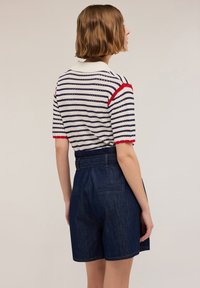 Raidallinen lyhythihainen paita, jossa on punaisia yksityiskohtia ja valkoinen kaulus, yhdistettynä korkeavyötäröisiin tummiin denim-shorteihin, joissa on sivutaskut.