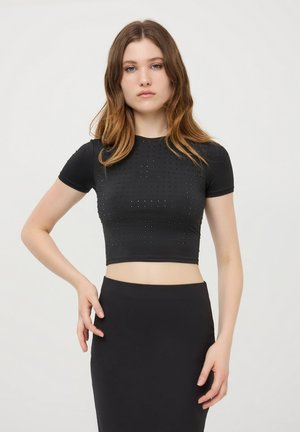 Cropped top nero realizzato in tessuto elasticizzato, con maniche corte e dettagli borchiati sul davanti. Il design è aderente e slanciato.