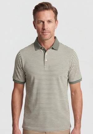 Man die een poloshirt met korte mouwen draagt met olijfgroene en witte horizontale strepen, een effen olijfgroene kraag en mouwboorden, staand tegen een effen achtergrond.