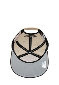 Casquette grise à visière plate, intérieur beige et accents noirs. Elle présente des logos imprimés et des coutures le long de la couronne et de la visière.