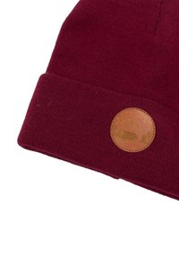 Burgundowa dzianinowa czapka z podwiniętym brzegiem i okrągłą brązową skórzaną naszywką z motywem sylwetek drzewa i zwierzęcia.