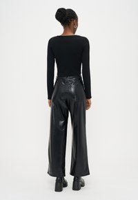 Top preto de mangas compridas combinado com calças pretas texturizadas de couro sintético, de cintura alta e perna larga. Botas pretas grossas de salto completam o visual.