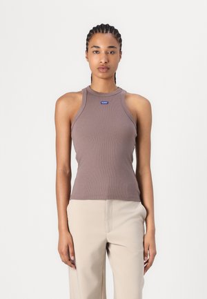 Débardeur en maille marron sans manches avec un col montant et une petite étiquette bleue au centre. À porter avec un pantalon beige clair.