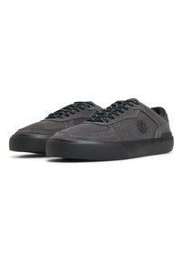 Gray suede sneakers with black rubber soles, contrasting blue laces, and subtle stitching details. Features a circular logo on the side.
