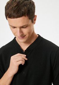 Sort sweater med høj krave og kort lynlås fortil. Stoffet er glat og let struktureret, hvilket giver en behagelig pasform.