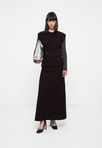 Burgunderfarbenes Zweiteiler-Outfit mit einem strukturierten Oberteil und grauen Ärmeln, kombiniert mit einer silbernen Clutch im Schlangenmuster und schwarzen High Heels.