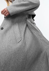 Grijze wolmix jas met een losse pasvorm, voorzien van een enkele knoop, zijzakken en een strikband detail voor een verstelbare pasvorm.