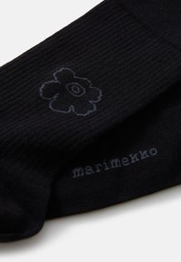 Calze nere con texture a costine, caratterizzate da un design di fiori blu scuro e il testo "marimekko" tessuto di lato.