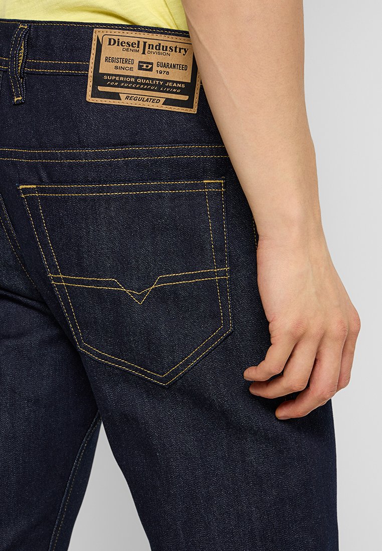 Dunkelblaue Jeans aus Denim mit einem Lederpatch, das "Diesel Industry" beschriftet ist. Mit gelben Nähten und einem markanten Design der Gesäßtasche.