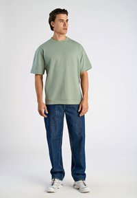 Jasnozielona bluza krótki rękaw, luźny krój, w połączeniu z szerokimi niebieskimi dżinsami i białymi trampkami z kolorowymi akcentami.