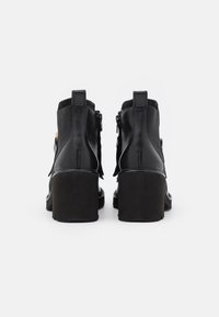 Černé kožené kotníkové boty s vysokým, robustním podpatkem. Mají zipové uzávěry a texturovanou tkaninovou část po stranách. Čistý, elegantní design.