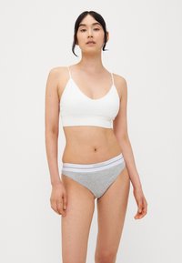Soutien-gorge blanc avec des bretelles fines et un décolleté en V profond, associé à une culotte grise avec une ceinture élastique blanche. Texture de tissu douce.