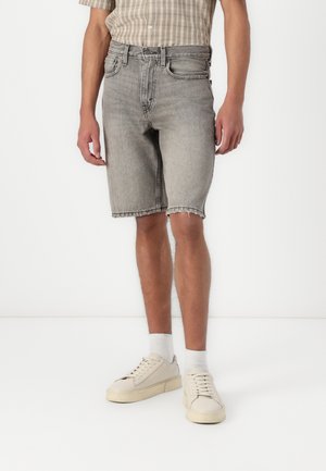 Grey denim shorts with a straight cut, raw hem, five pockets, and a classic waistband, paired with beige sneakers and white socks.