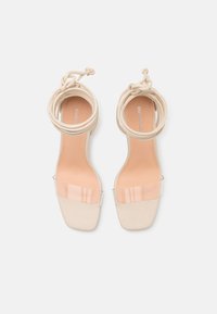 Nude högklackade sandaler med fyrkantig tå, klar vinylrem och inslagna ankelband. Slen yta och minimalistisk design.