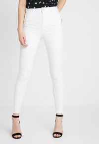 Jeans skinny de tiro alto blancos con una textura suave y un diseño ceñido, combinados con sandalias de tacón negras.