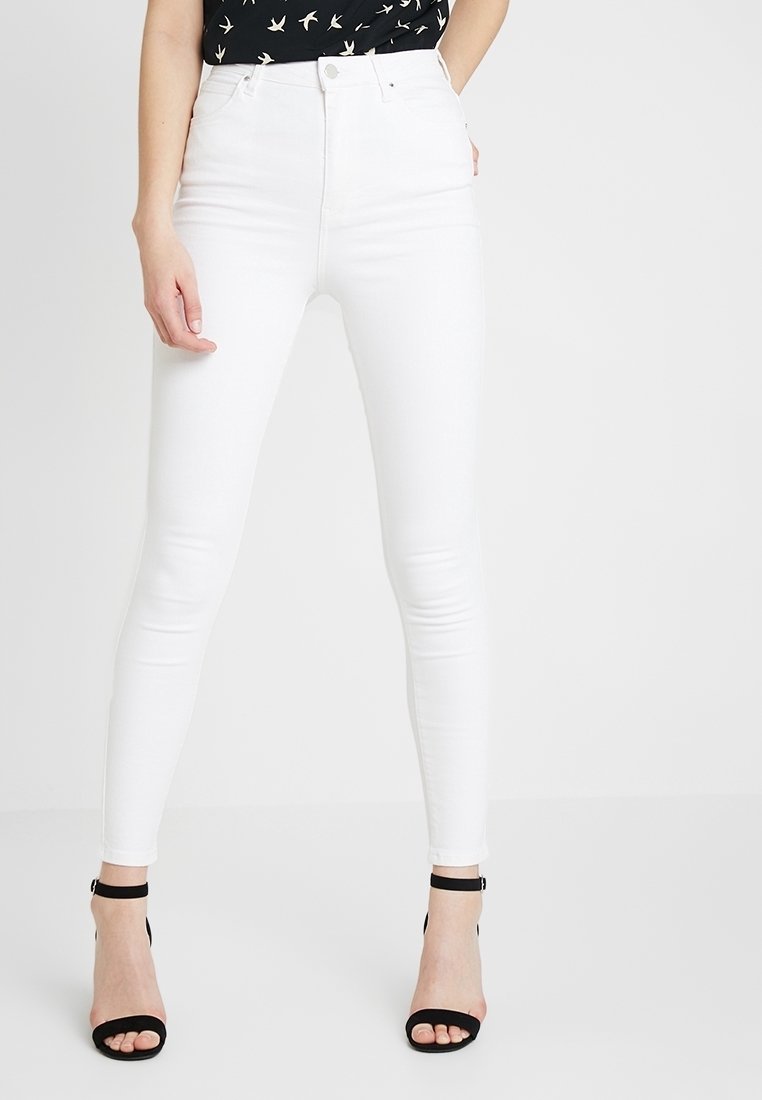 Jeans skinny de tiro alto blancos con una textura suave y un diseño ceñido, combinados con sandalias de tacón negras.