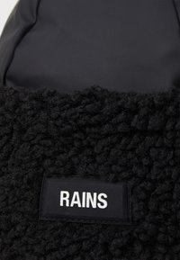 Črna torba za ramena, ki vsebuje teksturiran, puhast material in gladko oblogo, z pravokotno etiketo, na kateri je napisano "RAINS" v belem tisku.