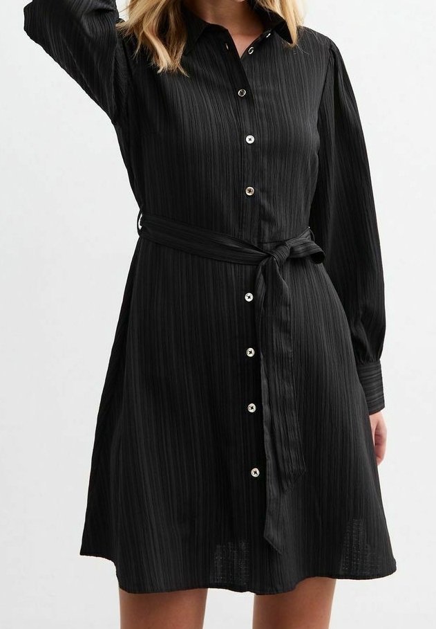 Czarna sukienka zapinana na guziki z kołnierzykiem, plisowaną fakturą, długimi rękawami i pasującym paskiem w talii. Akcenty w kolorze srebrnym.