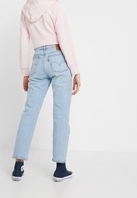 Jeans en denim bleu clair avec une coupe droite, taille haute et couture sur les poches arrière. Associés à un sweat à capuche court rose et des baskets marines.
