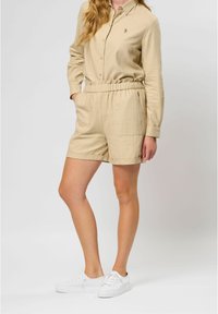 Beige, lichtgewicht, langemouwhemd met een knoopsluiting aan de voorkant en shorts met een elastische tailleband, gecombineerd met witte sneakers.