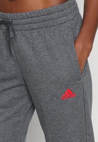 Grå joggingbukser lavet af bomuldsblandet stof med snøre i taljen, sidelommer og et rødt broderet Adidas-logo på venstre lår.