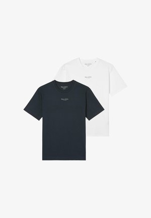 Uomo che indossa una semplice t-shirt bianca a maniche corte con un piccolo logo "Marc O'Polo" sul petto, abbinata a pantaloni beige, mani rilassate lungo i fianchi.