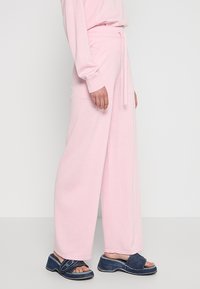 Lichtroze wijde broek van zachte stof, uitgerust met een koordje in de taille en zijzakken, in combinatie met donkerblauwe sandalen.