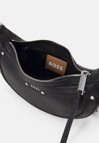 Černá kožená crossbody taška s texturou, se stříbrným zipem, kovovým logem a viditelným vnitřním štítkem s nápisem "BOSS" na hnědém poli.