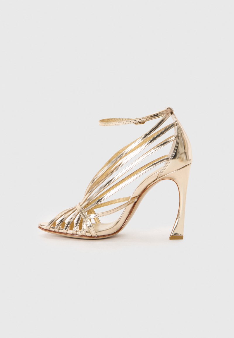 Golden strappy high-heeled sandal with a curved heel, open toe, and glossy finish. Features multiple metallic straps across the foot.