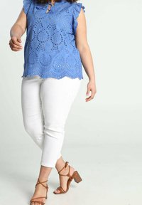 Blusa blu ricamata con maniche a cappuccio, caratterizzata da dettagli a taglio, abbinata a jeans bianchi aderenti e sandali con tacco strappy color sabbia.